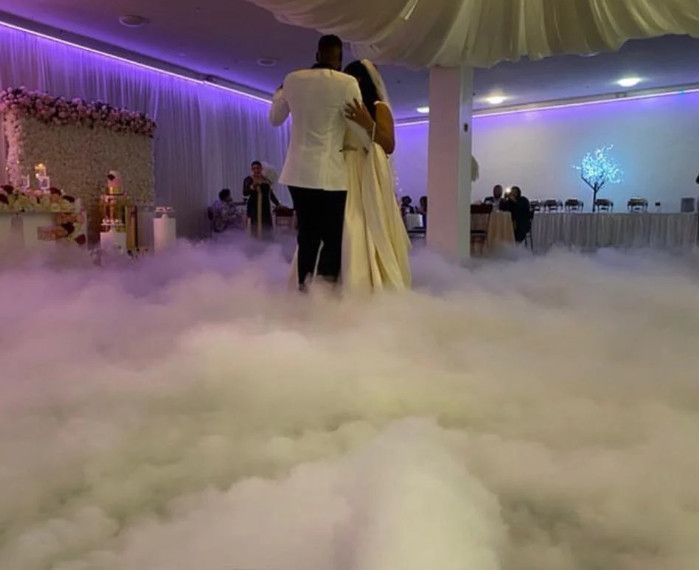 A bride and groom are dancing in the fog at their wedding reception.