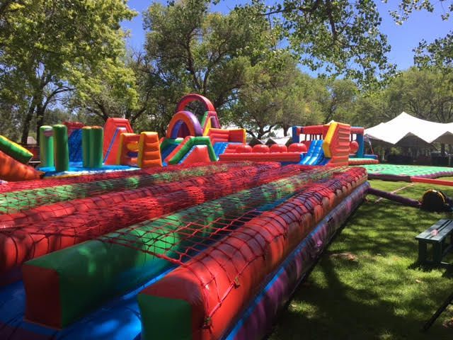 A large inflatable obstacle course in a park with trees in the background.