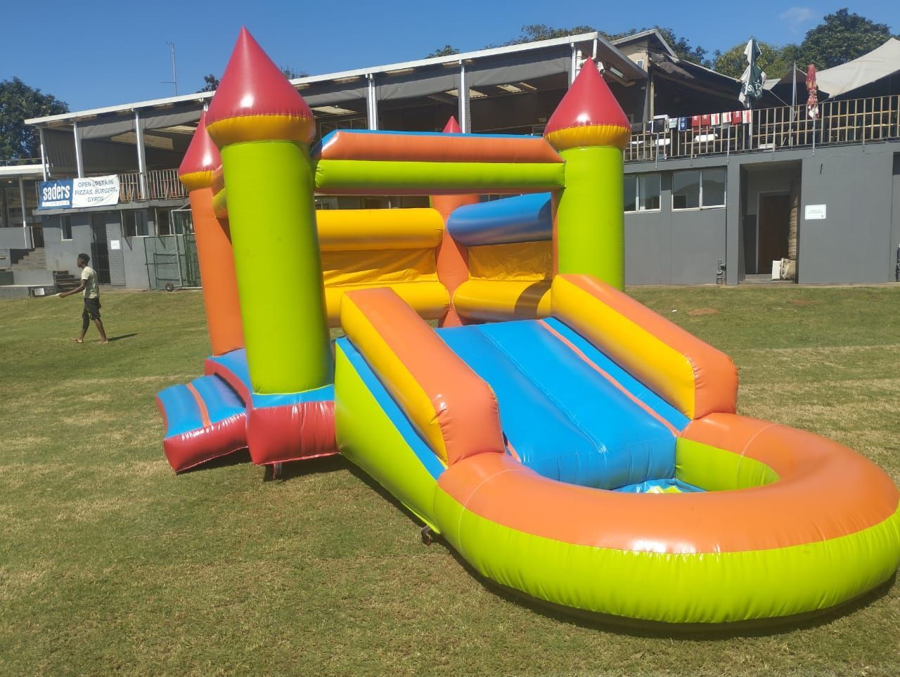A colorful bouncy castle with a slide is sitting in the grass in front of a building.