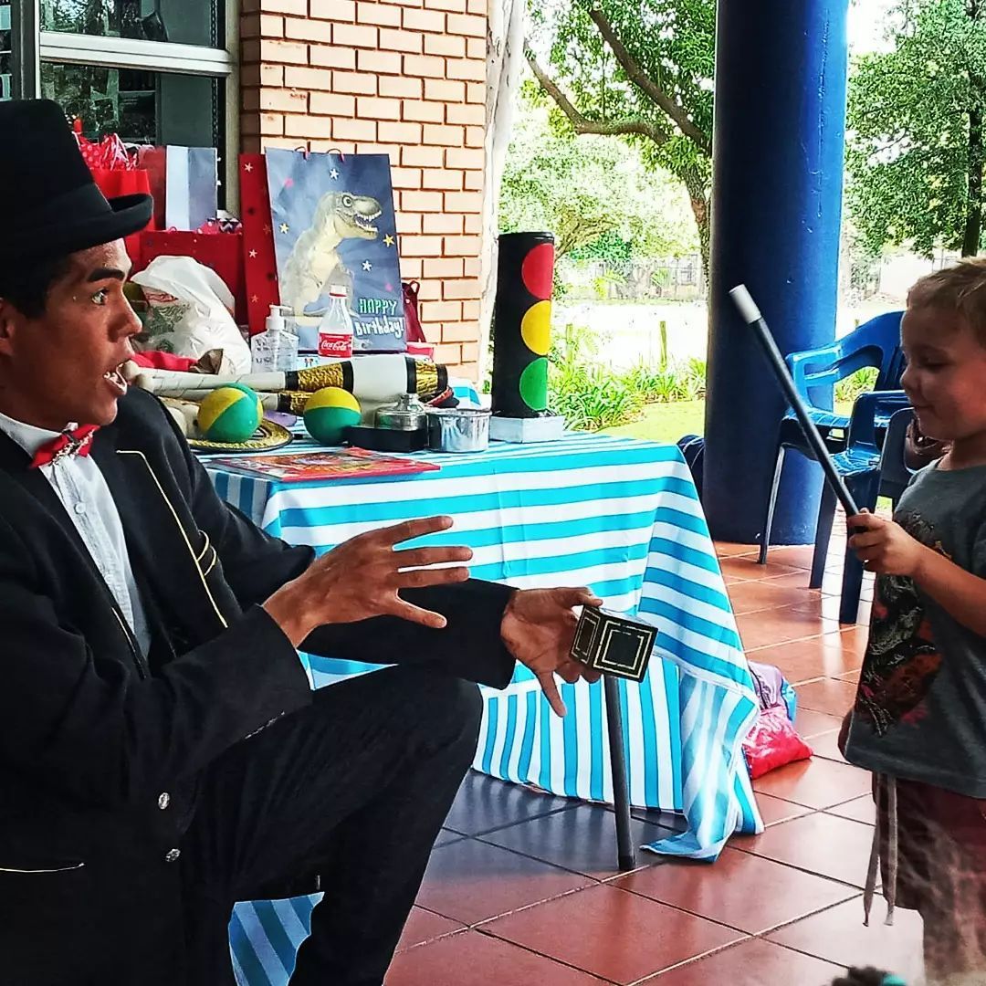A man in a top hat is performing a trick for a little boy