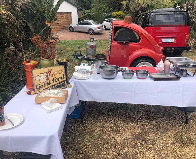 A red car is parked next to a table with a sign that says good food.