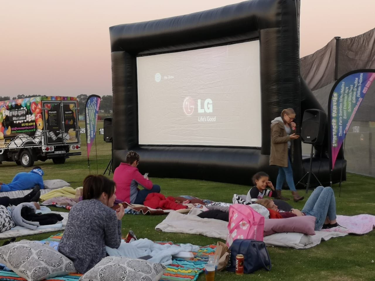 A group of people are sitting on blankets in front of an lg inflatable screen.