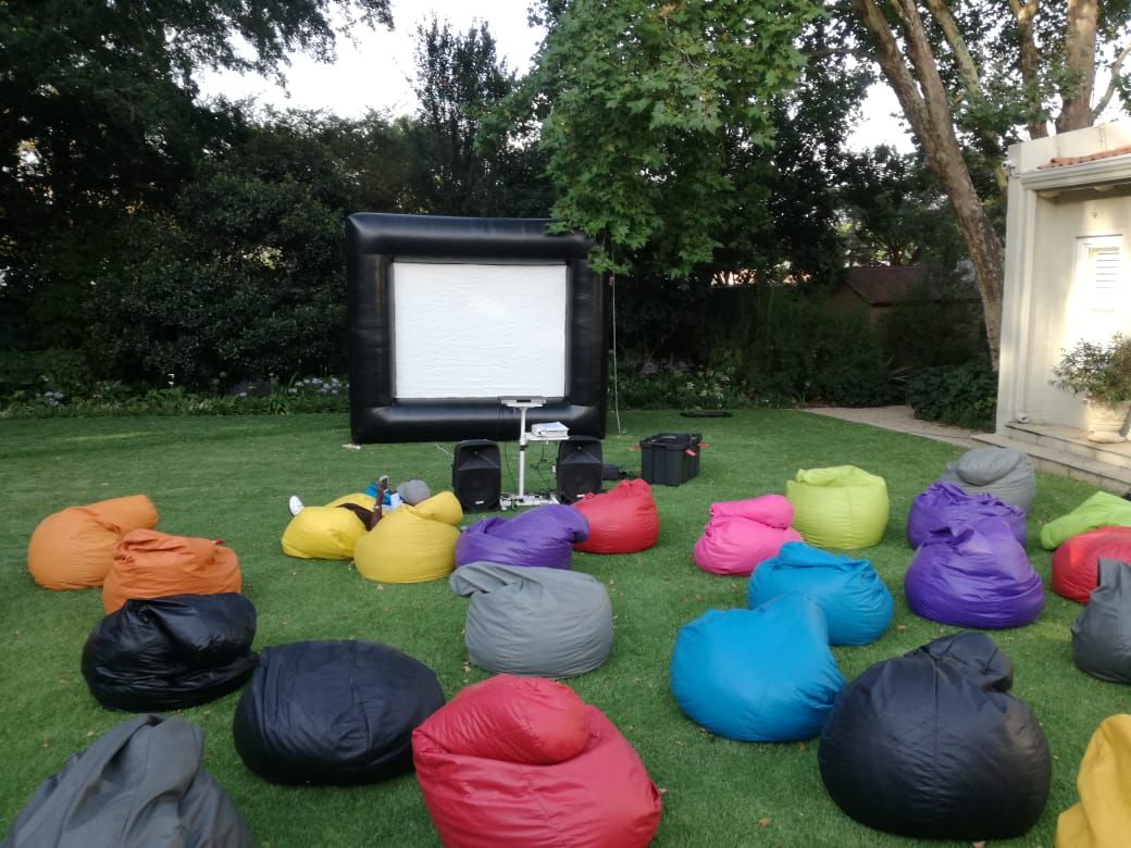 A bunch of bean bag chairs are sitting on the grass in front of an inflatable screen.