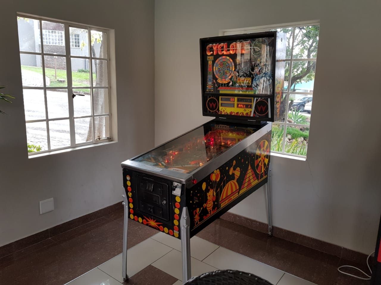 A pinball machine is sitting in a room next to a window.