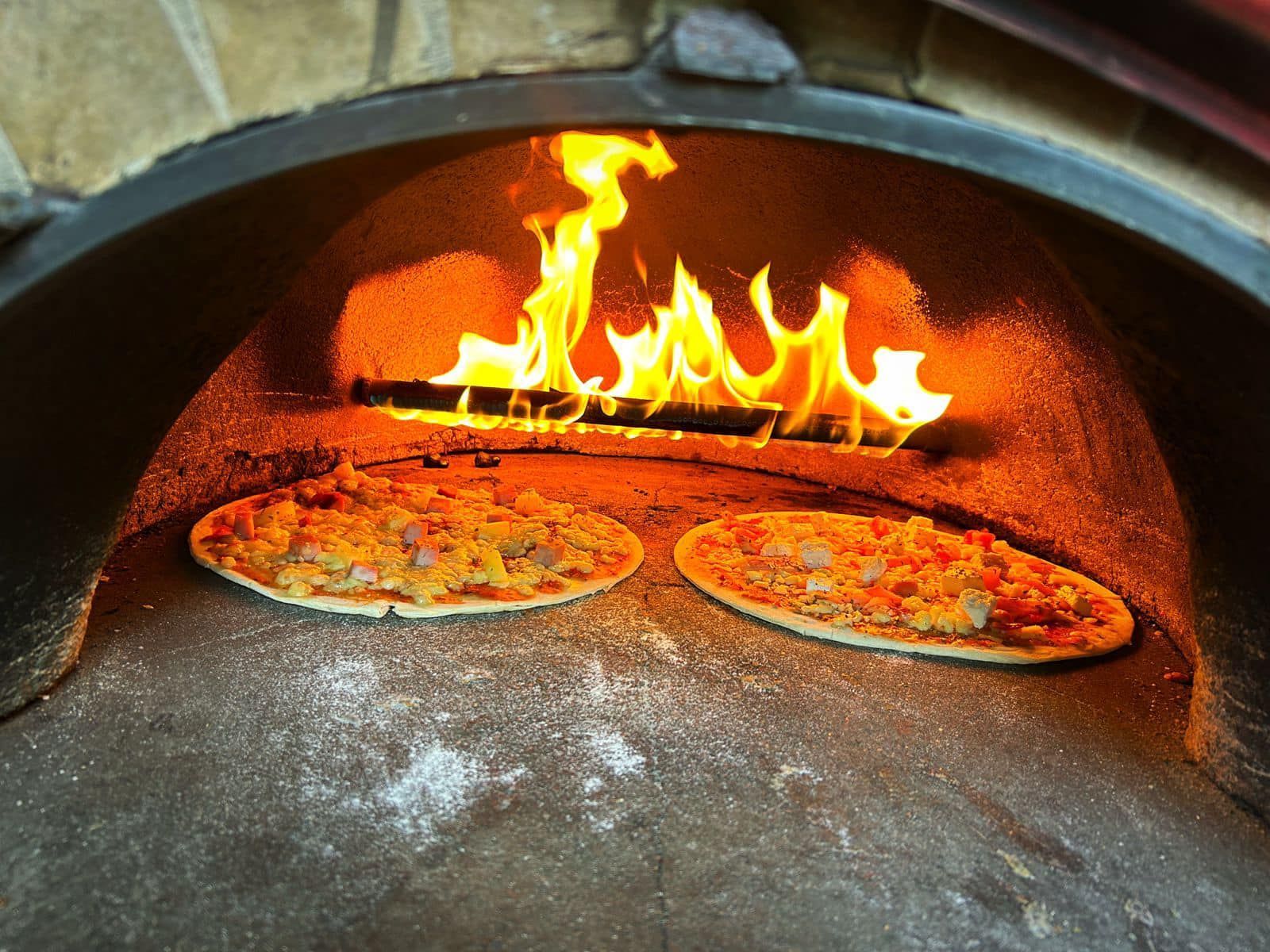 Two pizzas are cooking in a wood fired oven