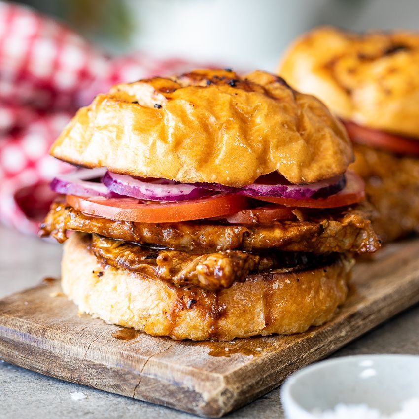 A close up of a chicken sandwich on a wooden cutting board.