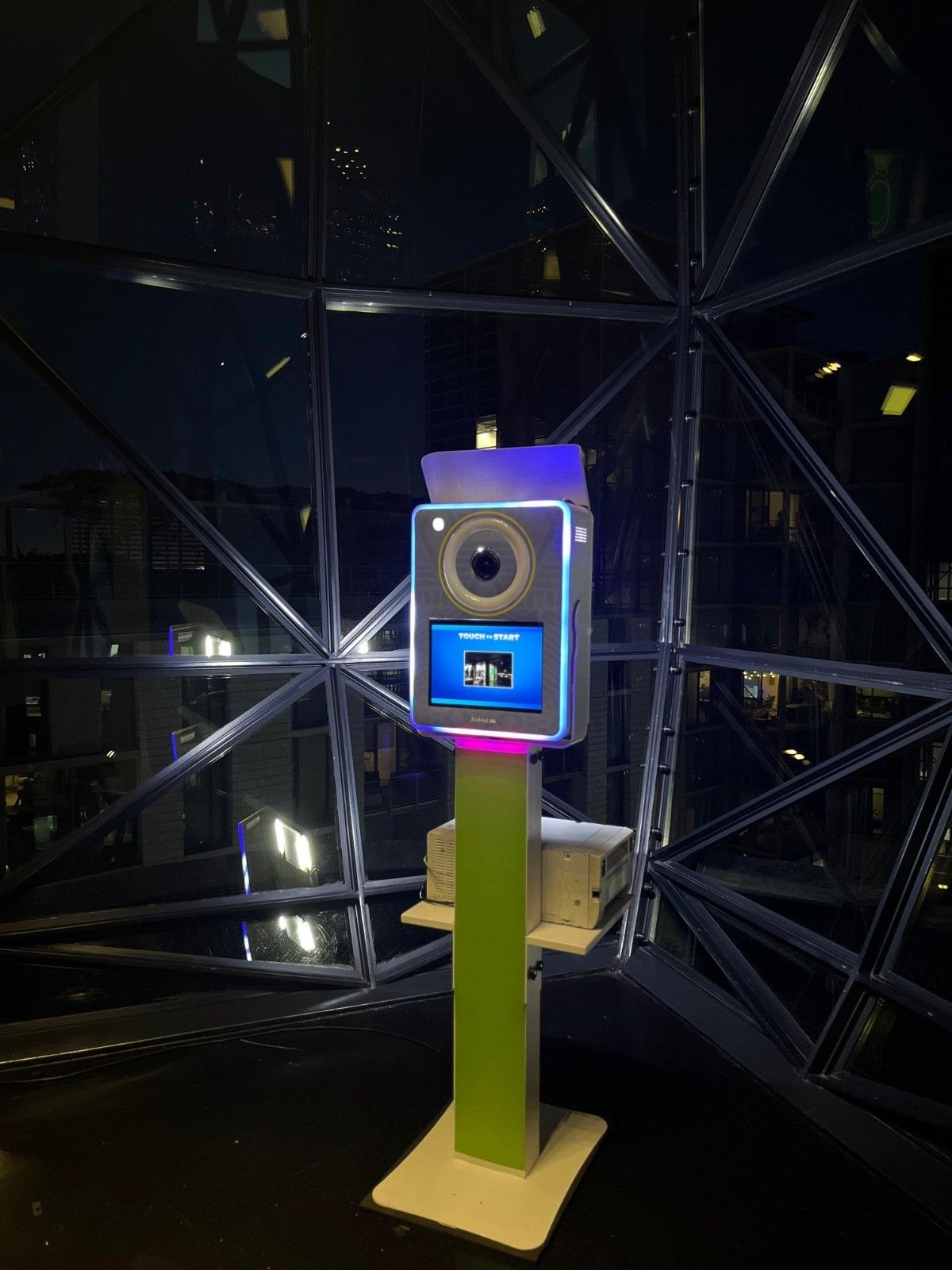 A photo booth is lit up at night in front of a glass dome.