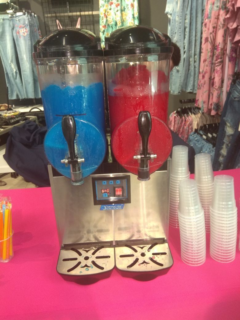 A slush machine is sitting on a pink table next to plastic cups.