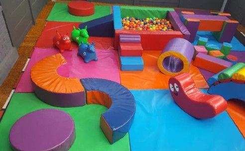 A colorful soft play area with a ball pit and toys.