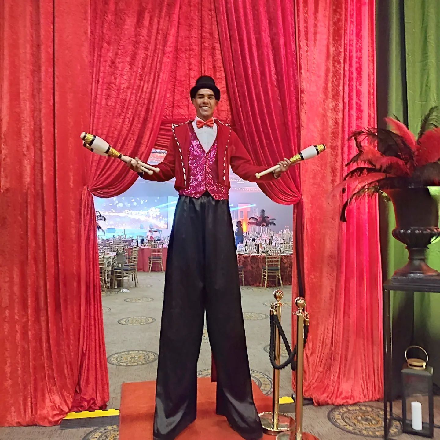 A man on stilts is standing in front of a red curtain.
