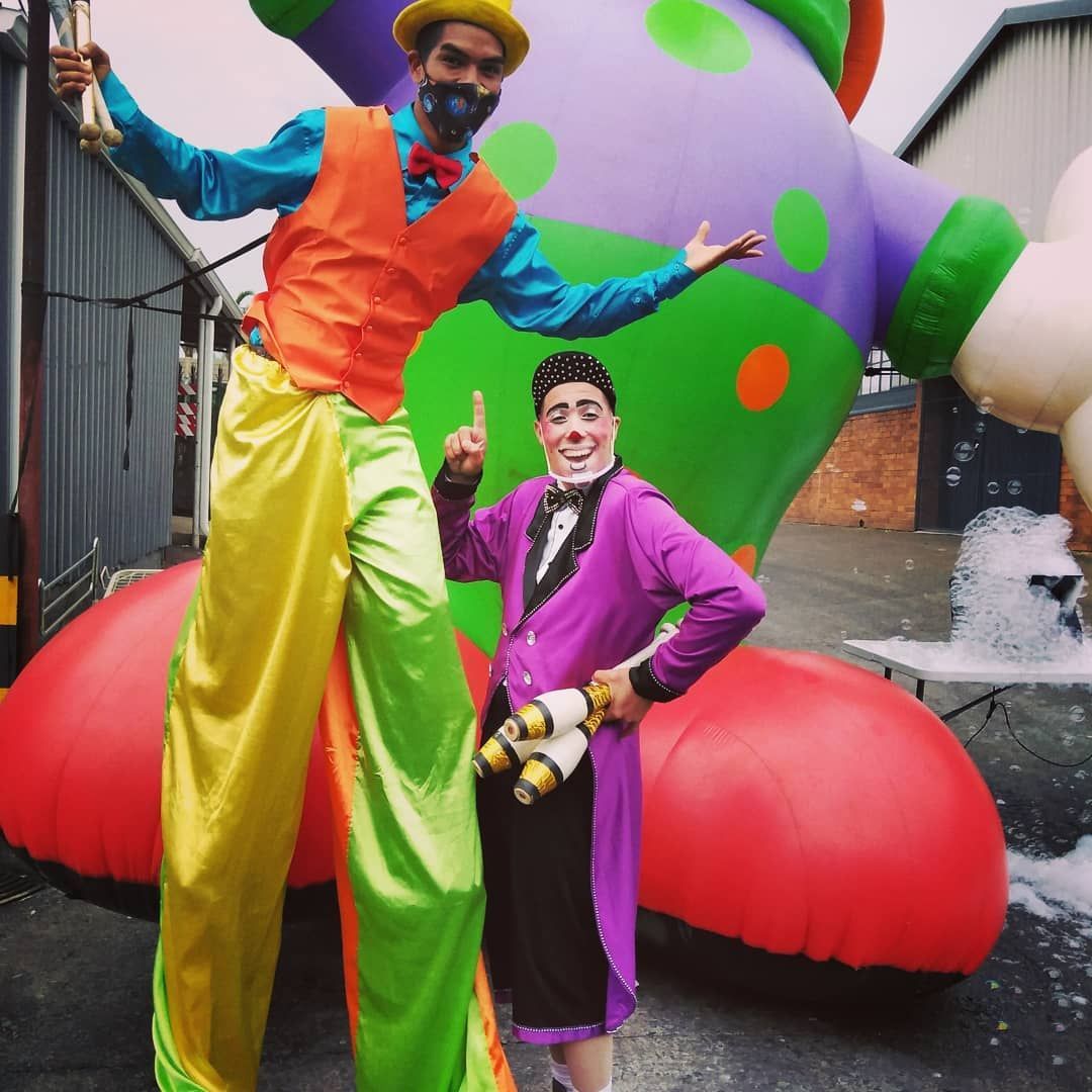 A clown on stilts stands next to another clown