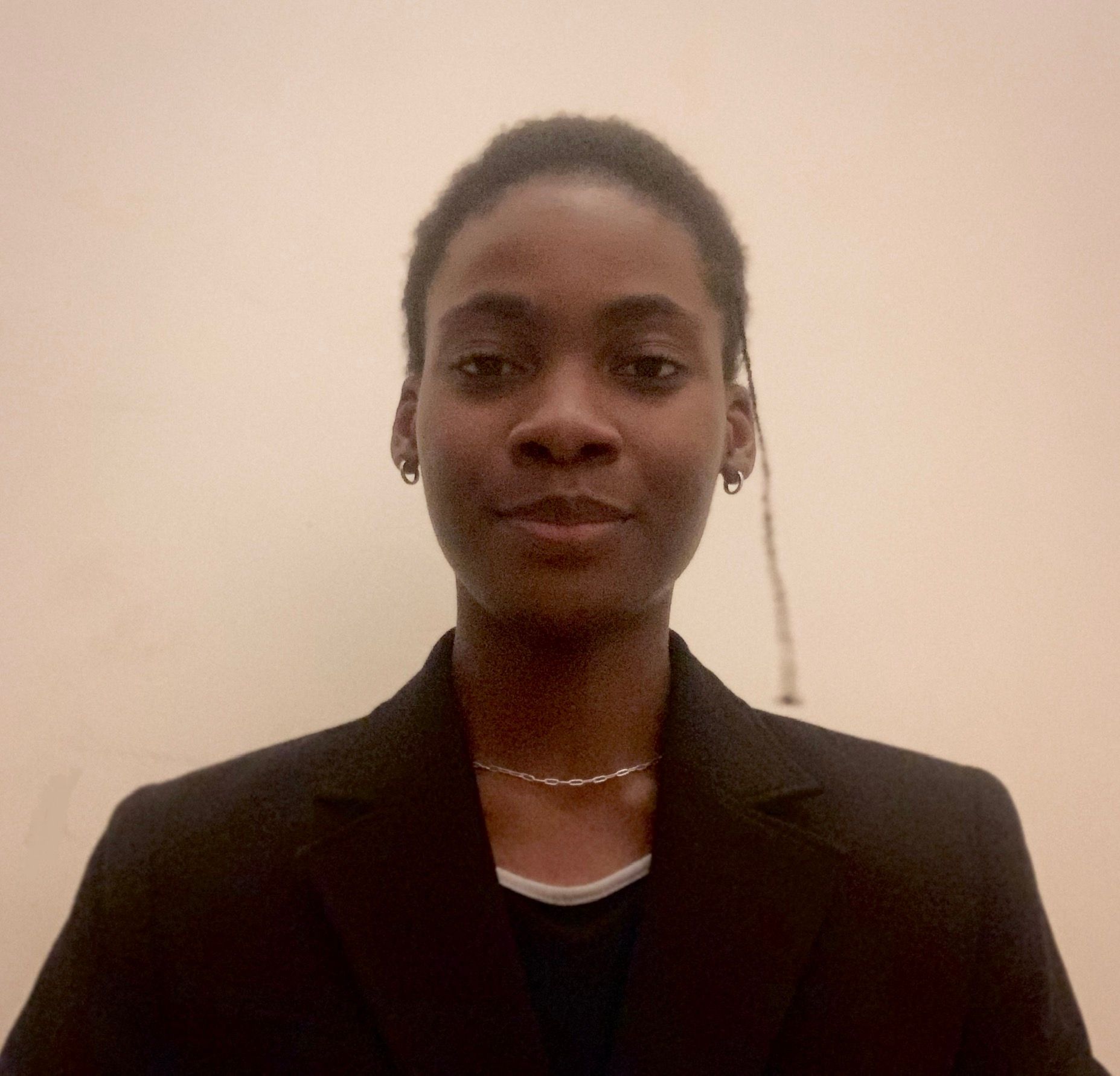 A woman wearing a black jacket and a necklace is smiling for the camera.