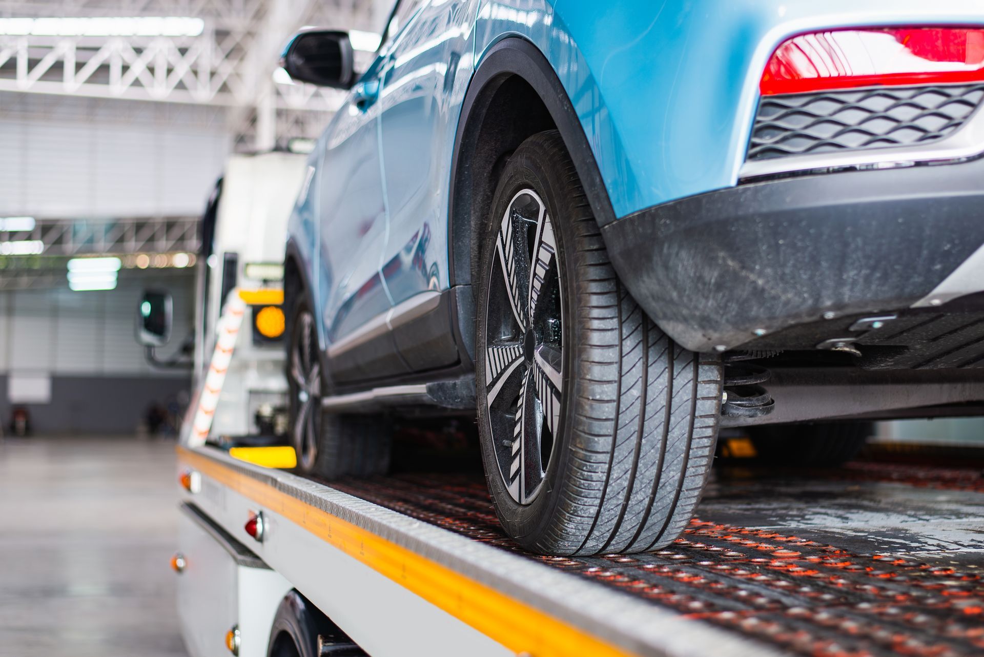 Blue car on a tow truck platform in a garage, with a wheel secured by a strap