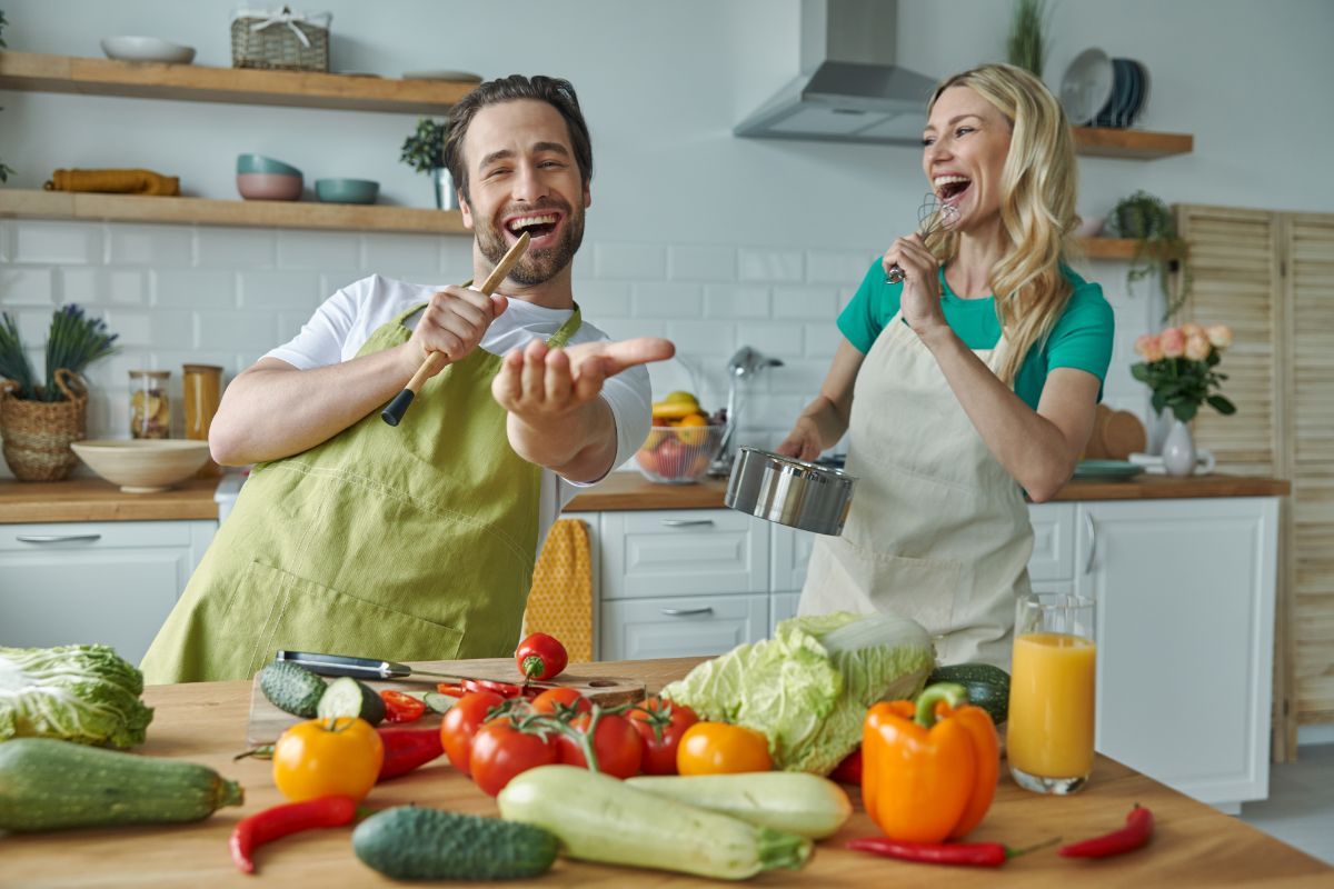 Coppia che canta e balla in cucina, cucinando le verdure.