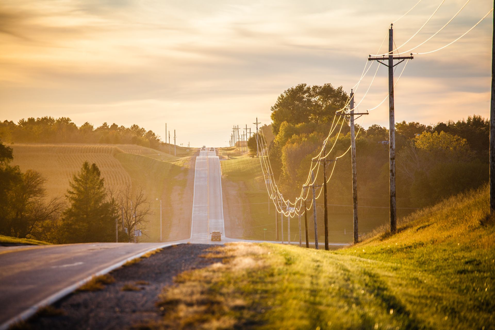 A car is driving down an empty country road at sunset.