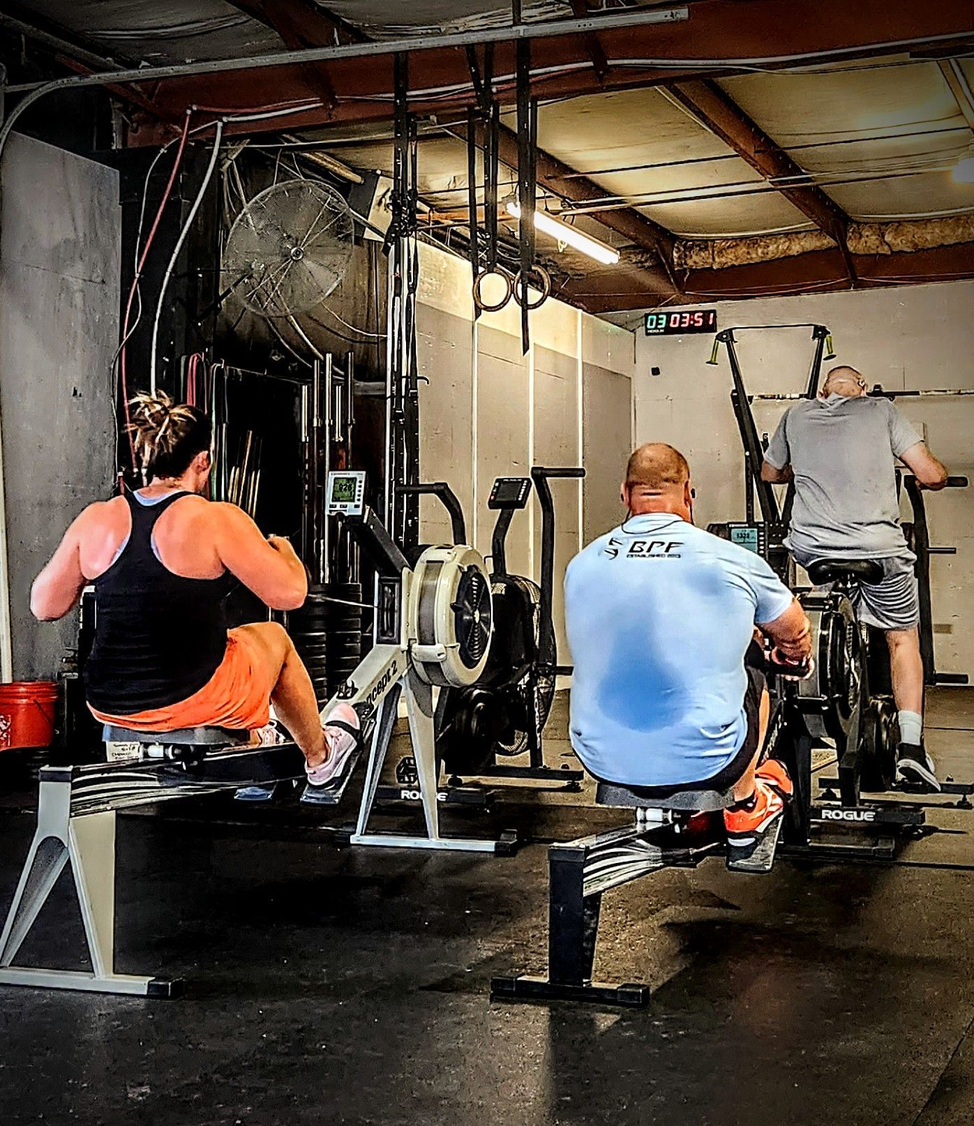 A man wearing a shirt that says tbc is riding a bike in a gym
