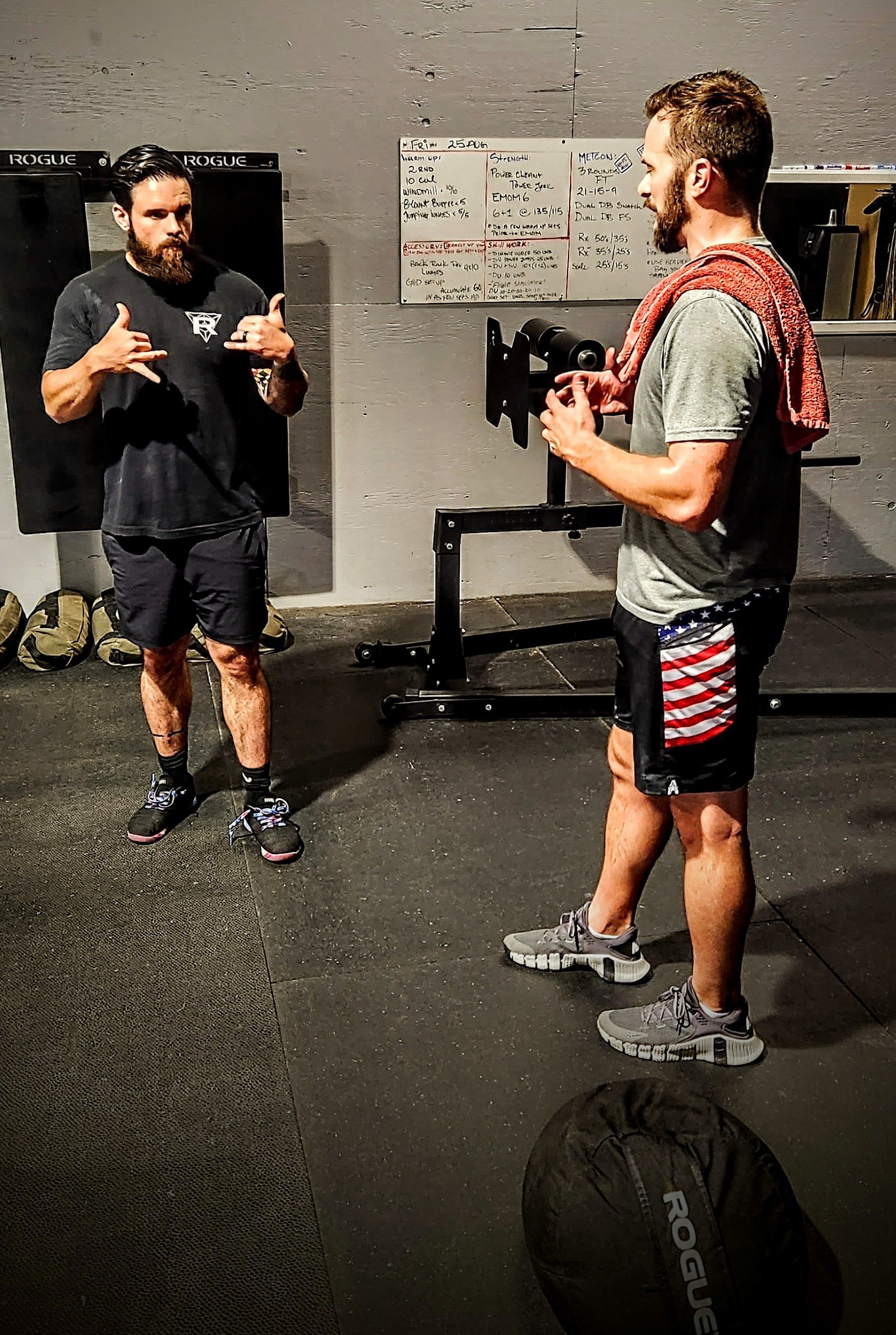 Two men are standing next to each other in a gym talking to each other.