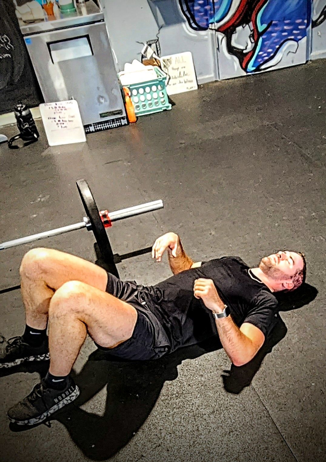 A man is laying on the floor with a barbell in a gym.