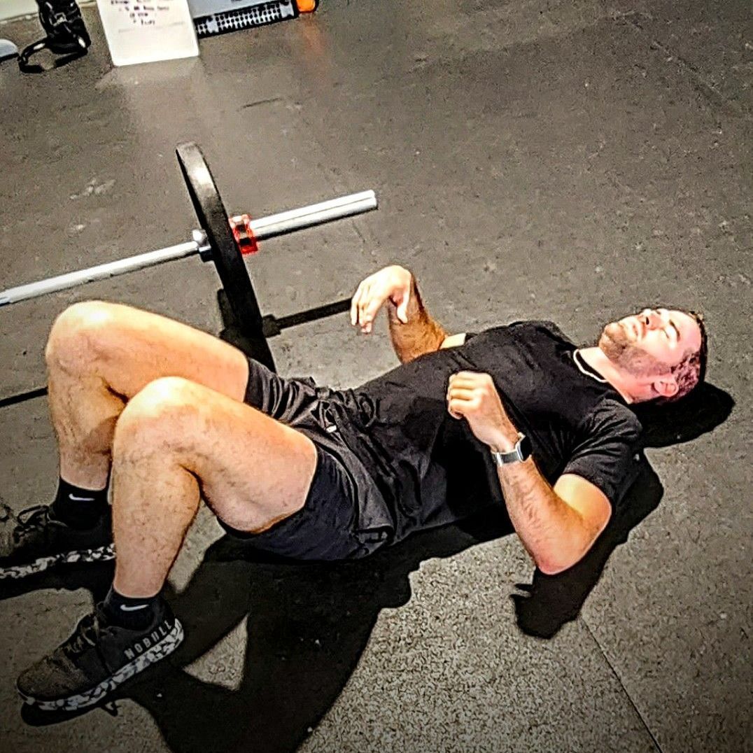 A man is laying on the floor with a barbell on his back.