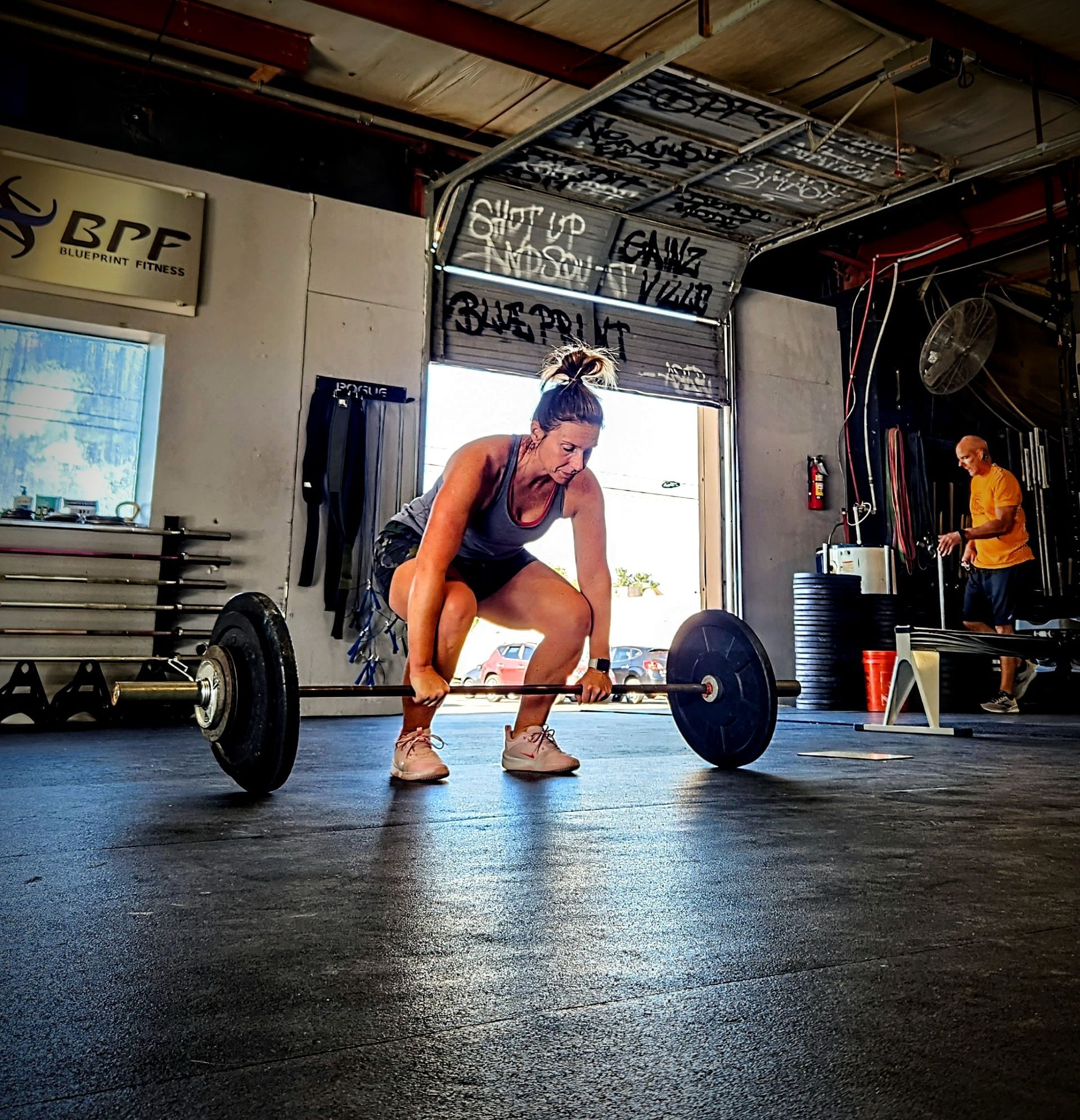 A woman is squatting down to lift a barbell in a gym