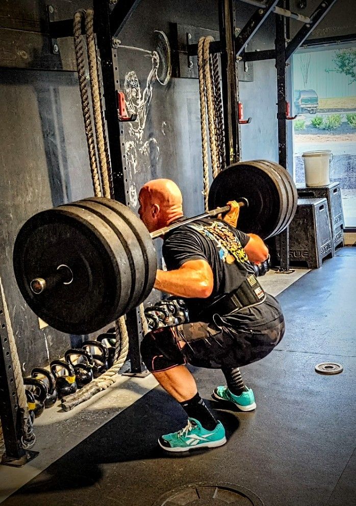 A man is squatting with a barbell over his head in a gym.