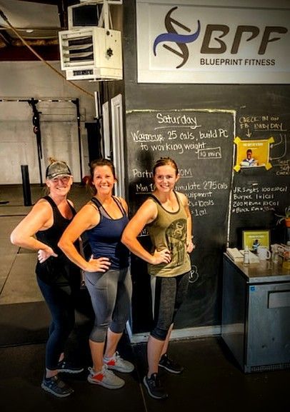 Three women are standing in front of a chalkboard in a gym.