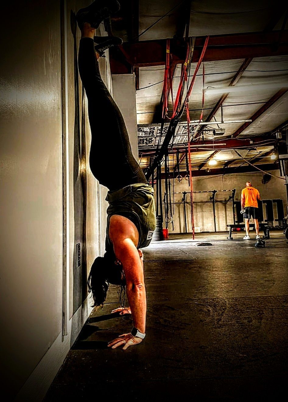 A woman is doing a handstand against a wall in a gym.