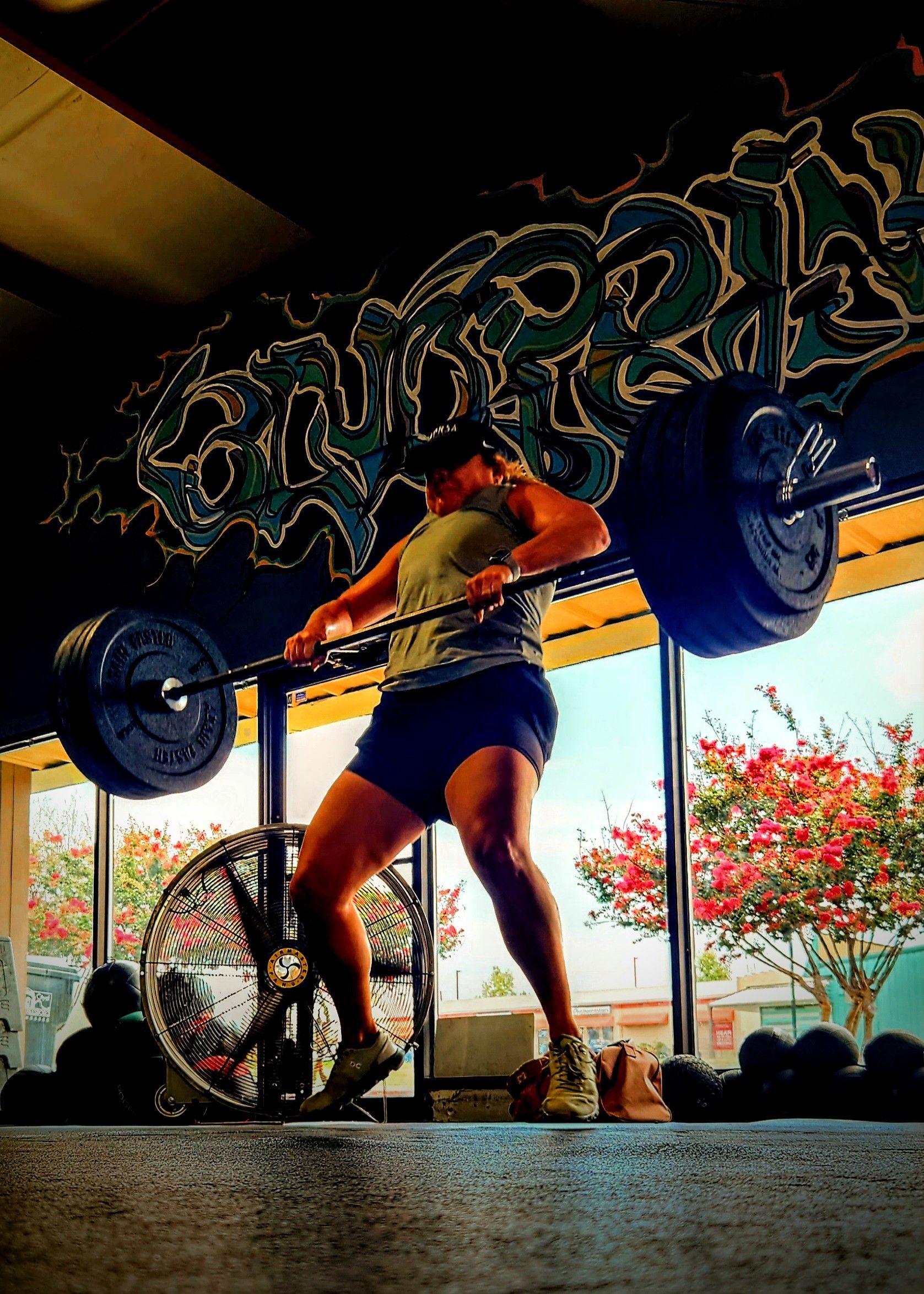 A woman is squatting with a barbell in a gym with graffiti on the wall behind her.