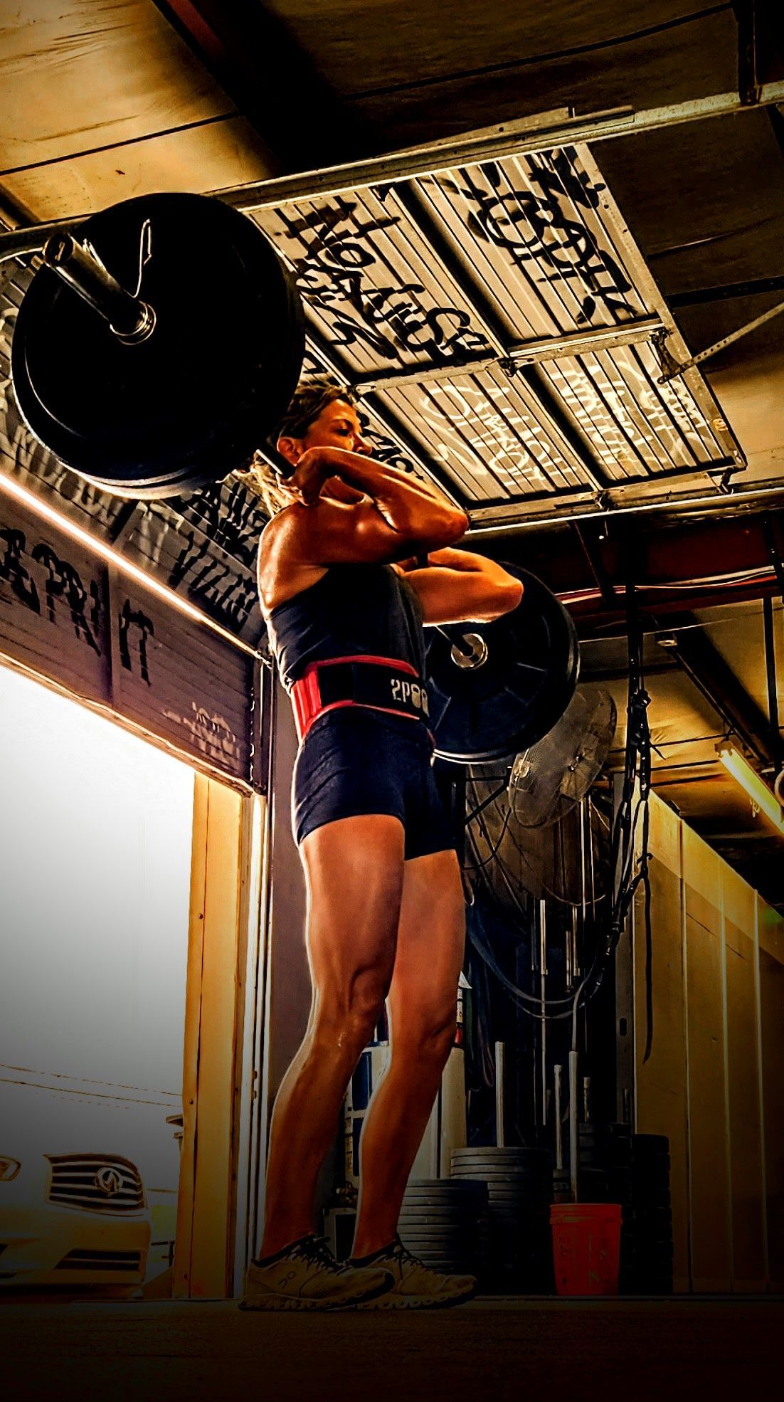 A woman is lifting a barbell over her head in a gym.