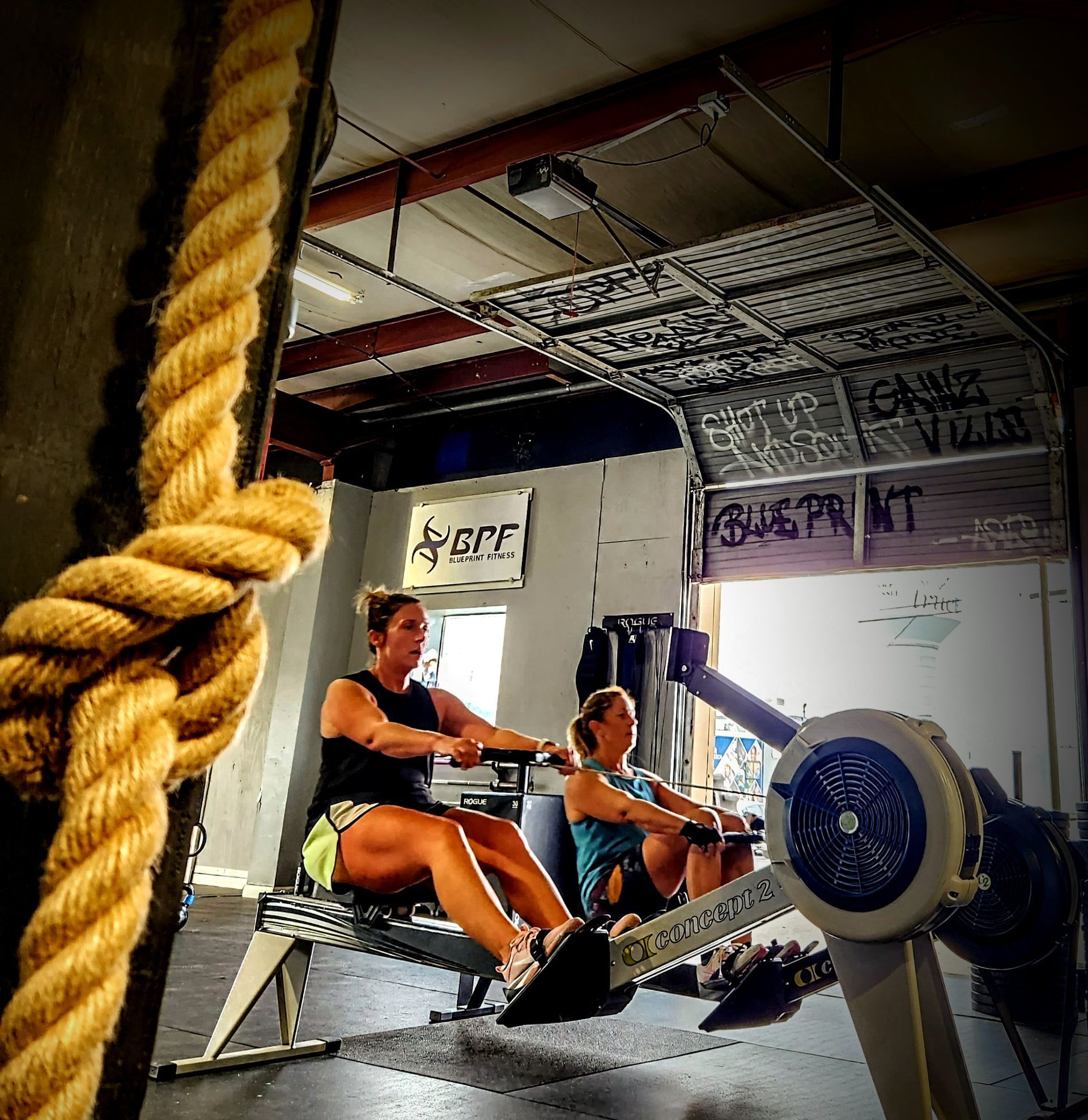 Two women are rowing in a gym with a sign that says rope