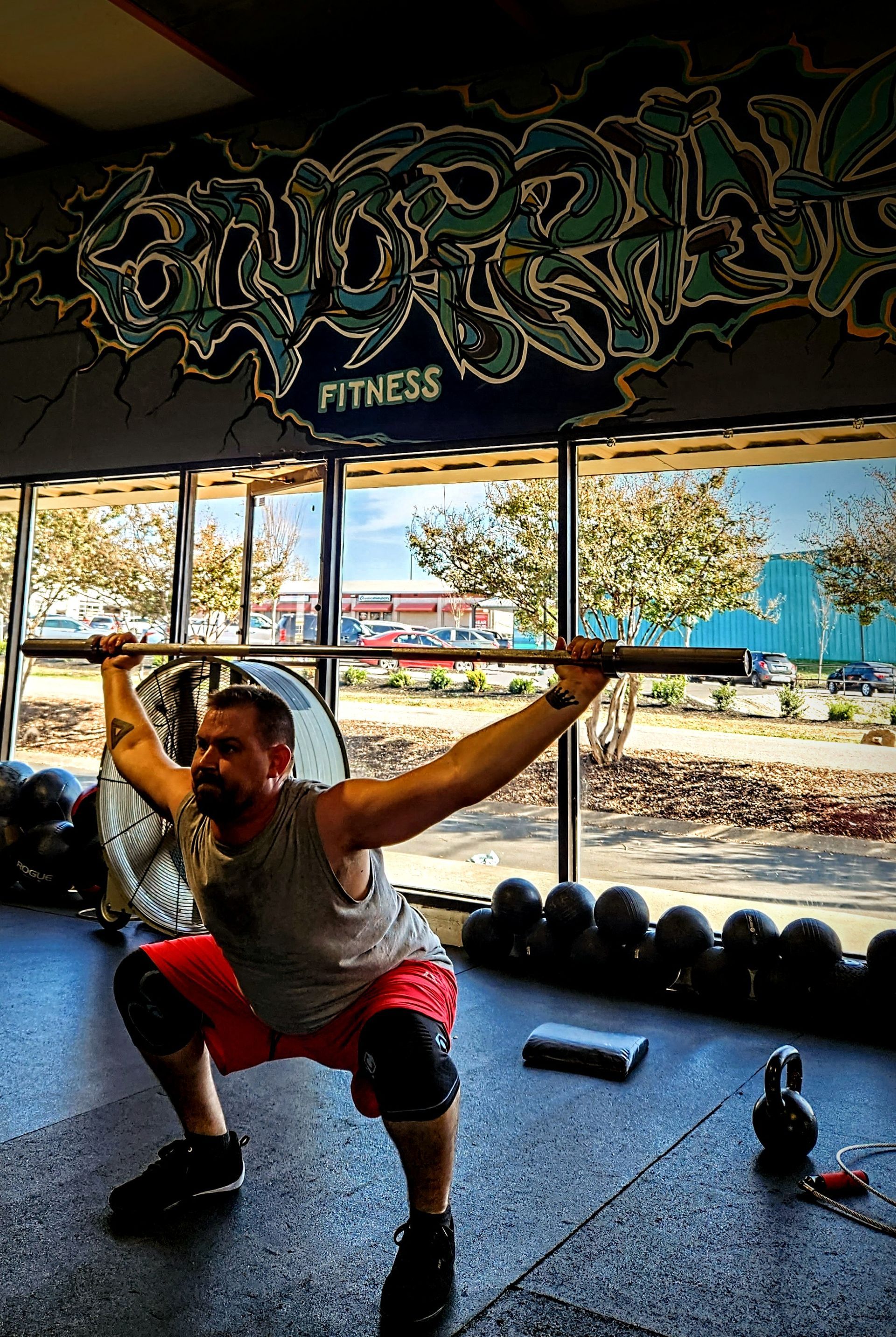 A man is squatting with a barbell over his head in a gym.