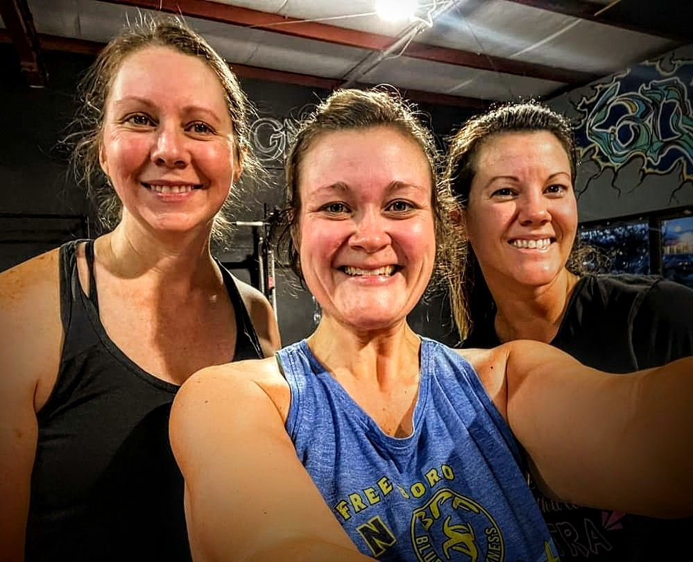 Three women are posing for a selfie in a gym.