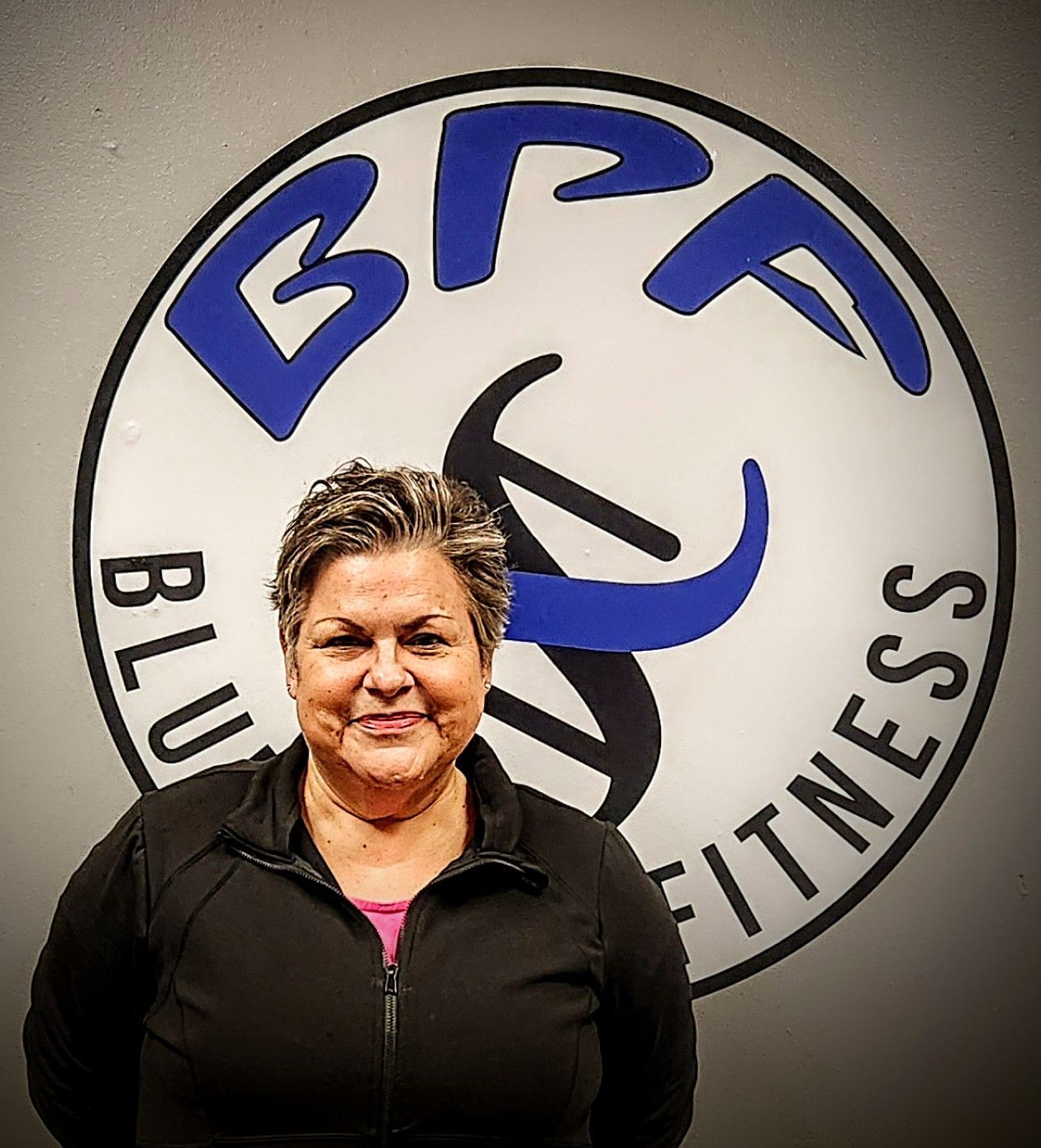A woman stands in front of a bfp fitness logo