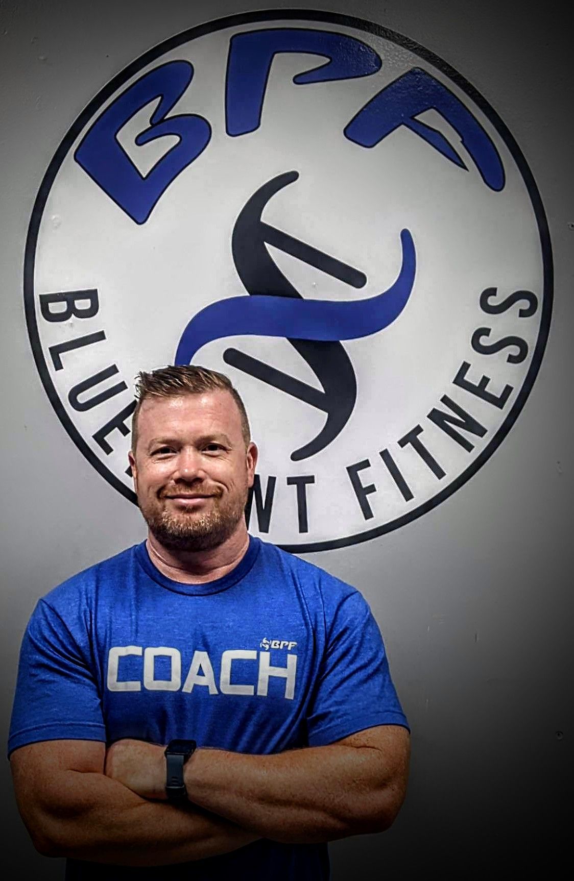 A man in a blue shirt is standing in front of a logo for a gym.