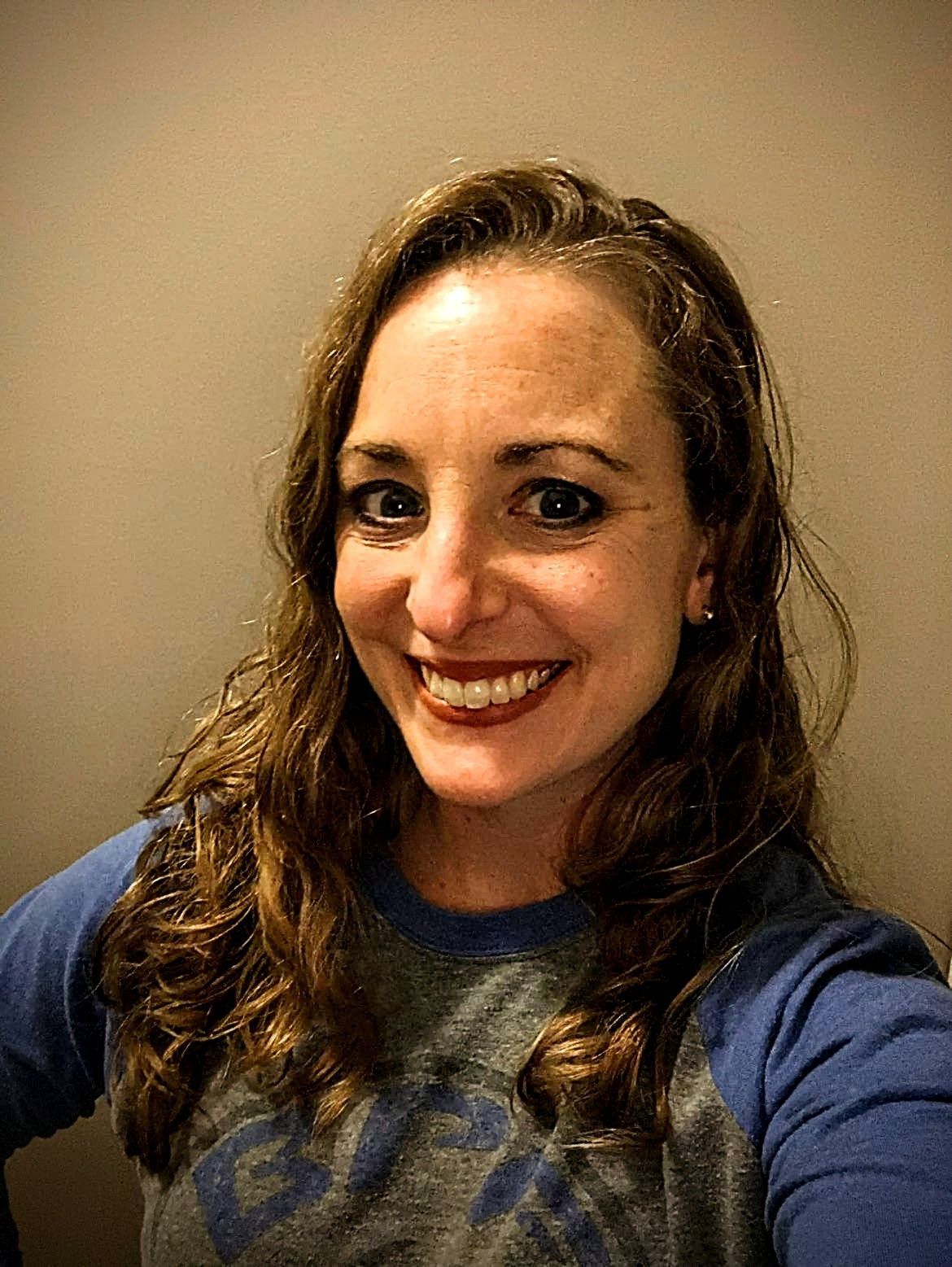 A woman in a blue shirt is smiling and taking a selfie.