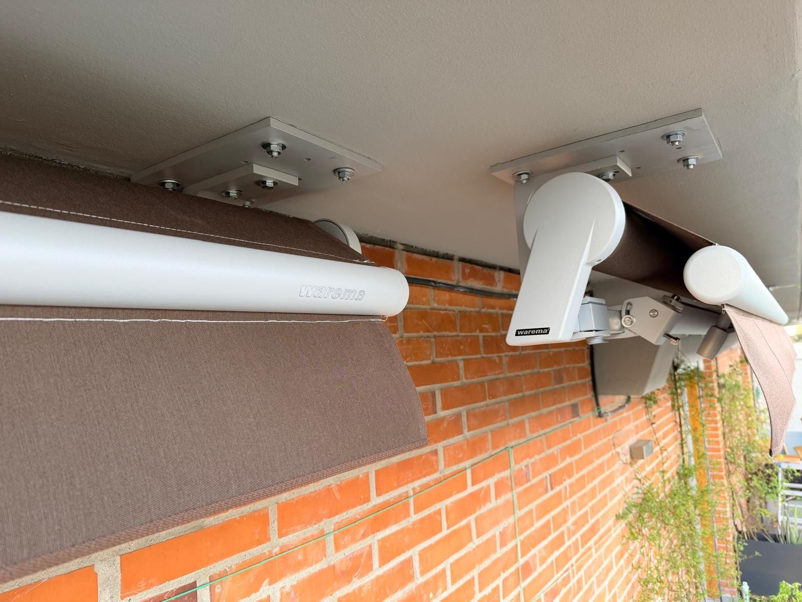 Tende da sole marroni e bianche fissate a un soffitto bianco sopra un muro di mattoni rossi.