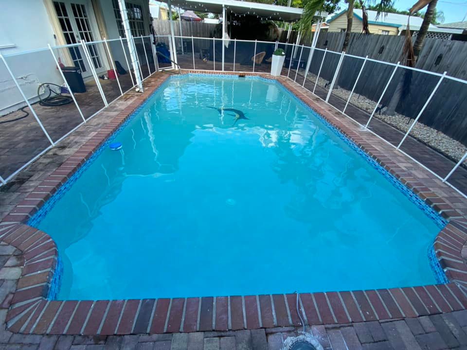 A large swimming pool with a fence around it and a brick border.