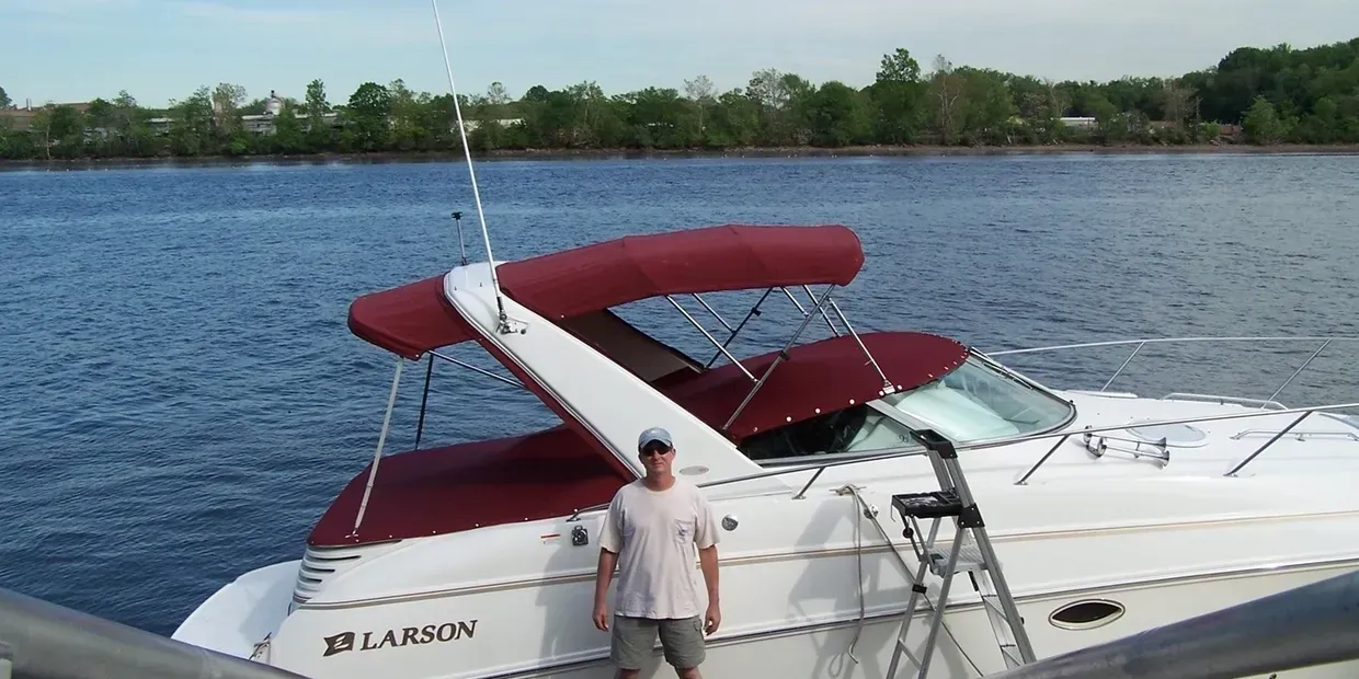 White motorboat with blue canopy docked among boats at a marina on a calm day