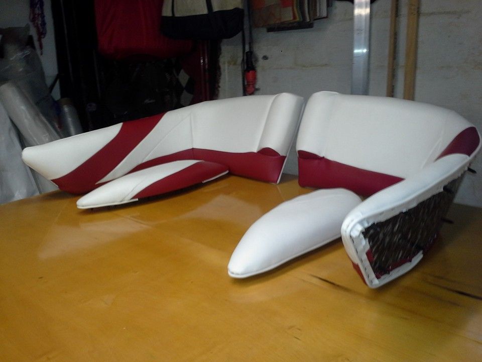 Classic wooden motorboat with tan cushions docked on the water, with larger yachts in the background
