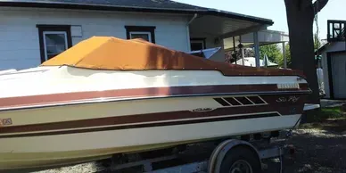 White and maroon speedboat with orange cover parked beside a house in a driveway