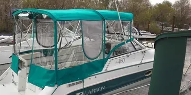 White and teal cabin cruiser covered with a teal canopy, docked beside a concrete seawall.