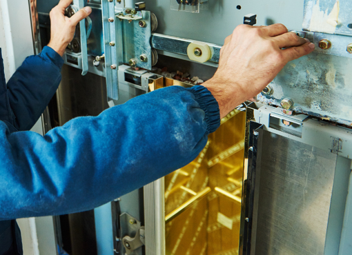 Les mains d'un technicien ajustent une machine industrielle bleue munie d'un protecteur de sécurité jaune.