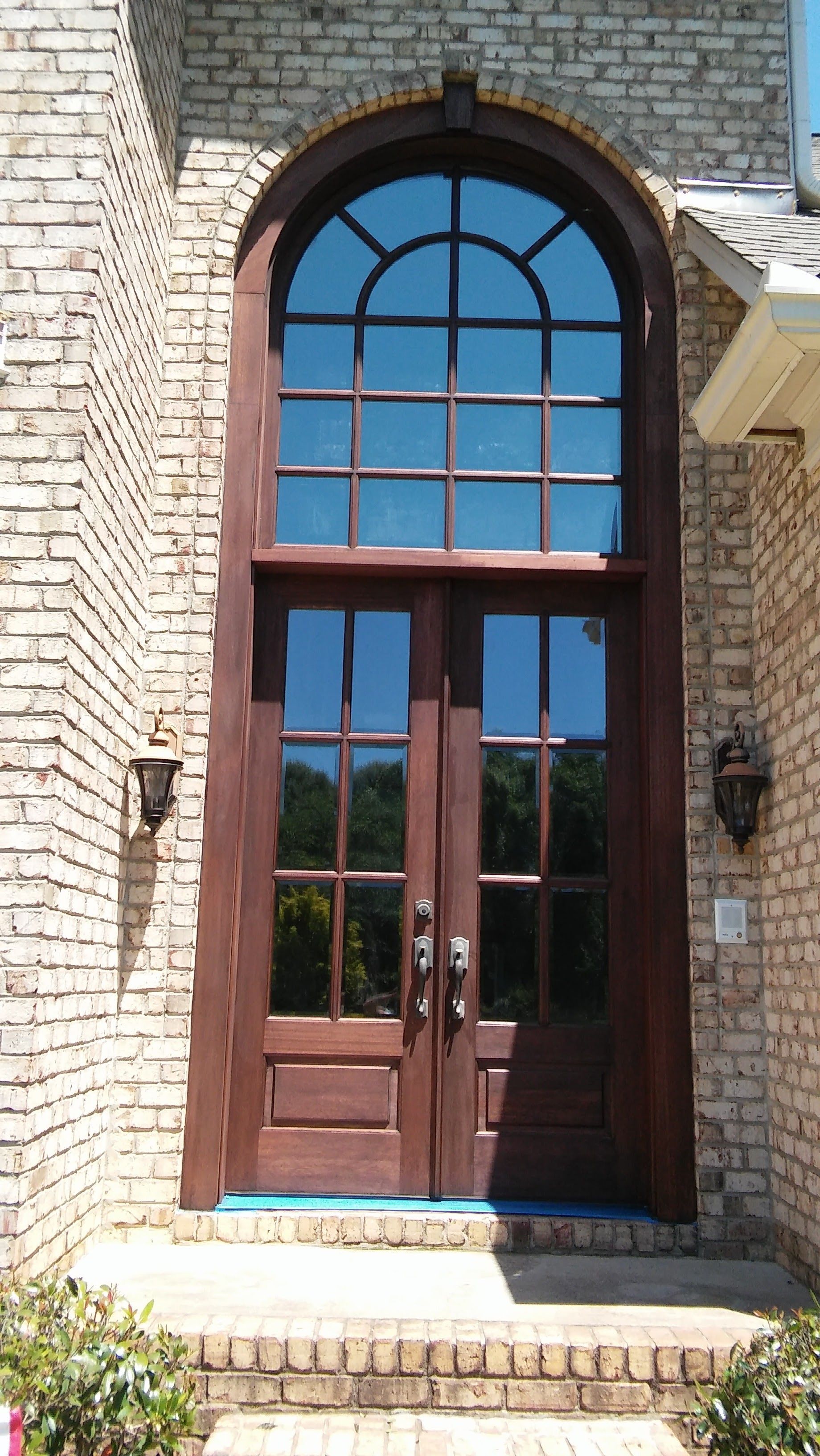 Brick home entrance with arched window above double doors; dark wood trim and sconces.