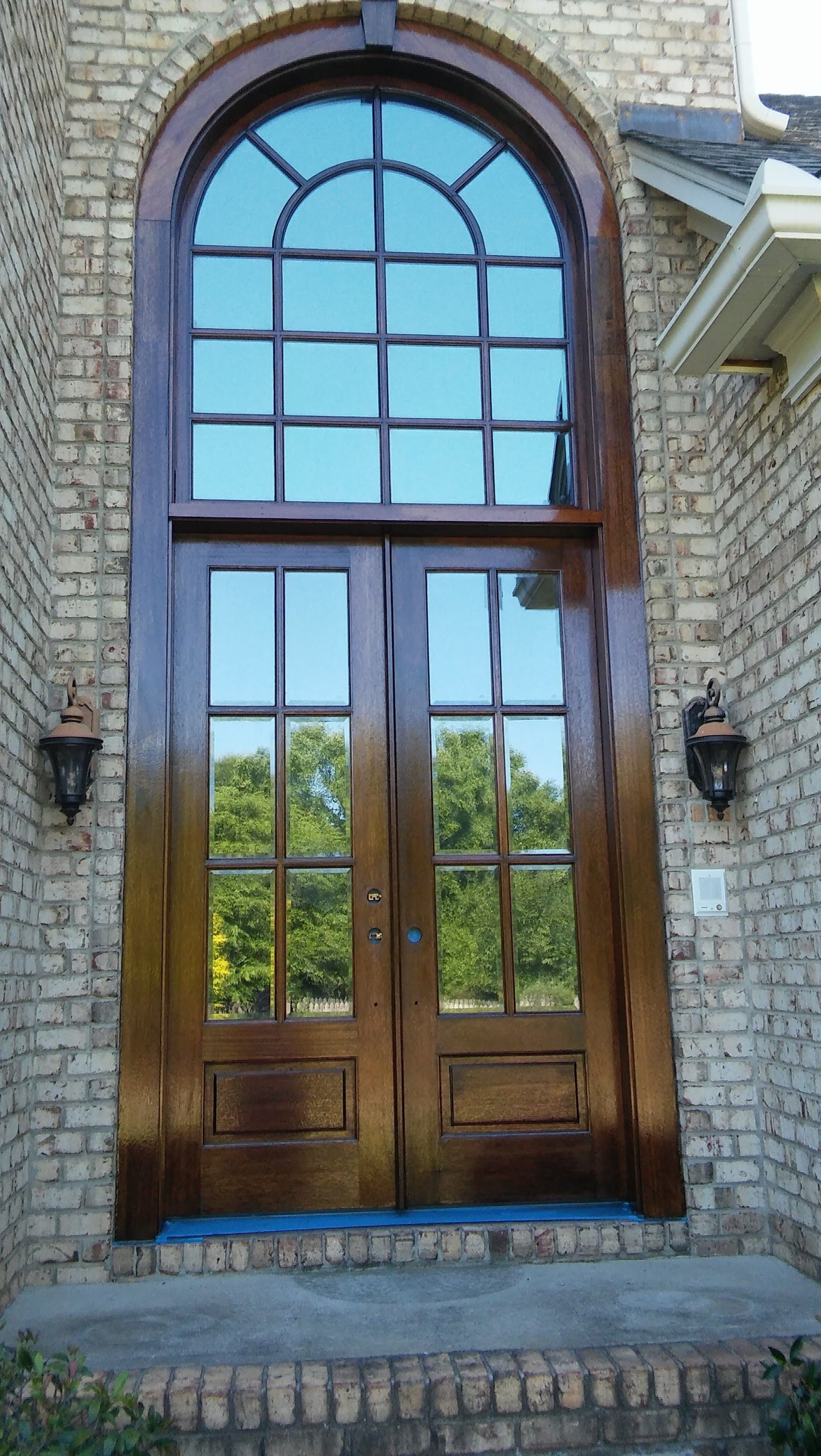 Tall wooden double doors with arched window above, set in brick.