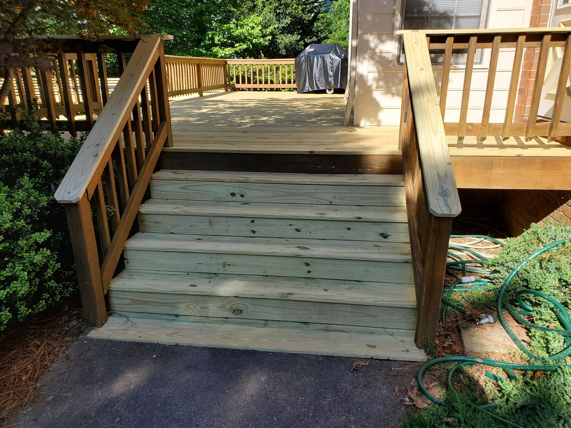 Wooden deck with steps, railings, and a partially covered grill. Green steps and brown deck boards.