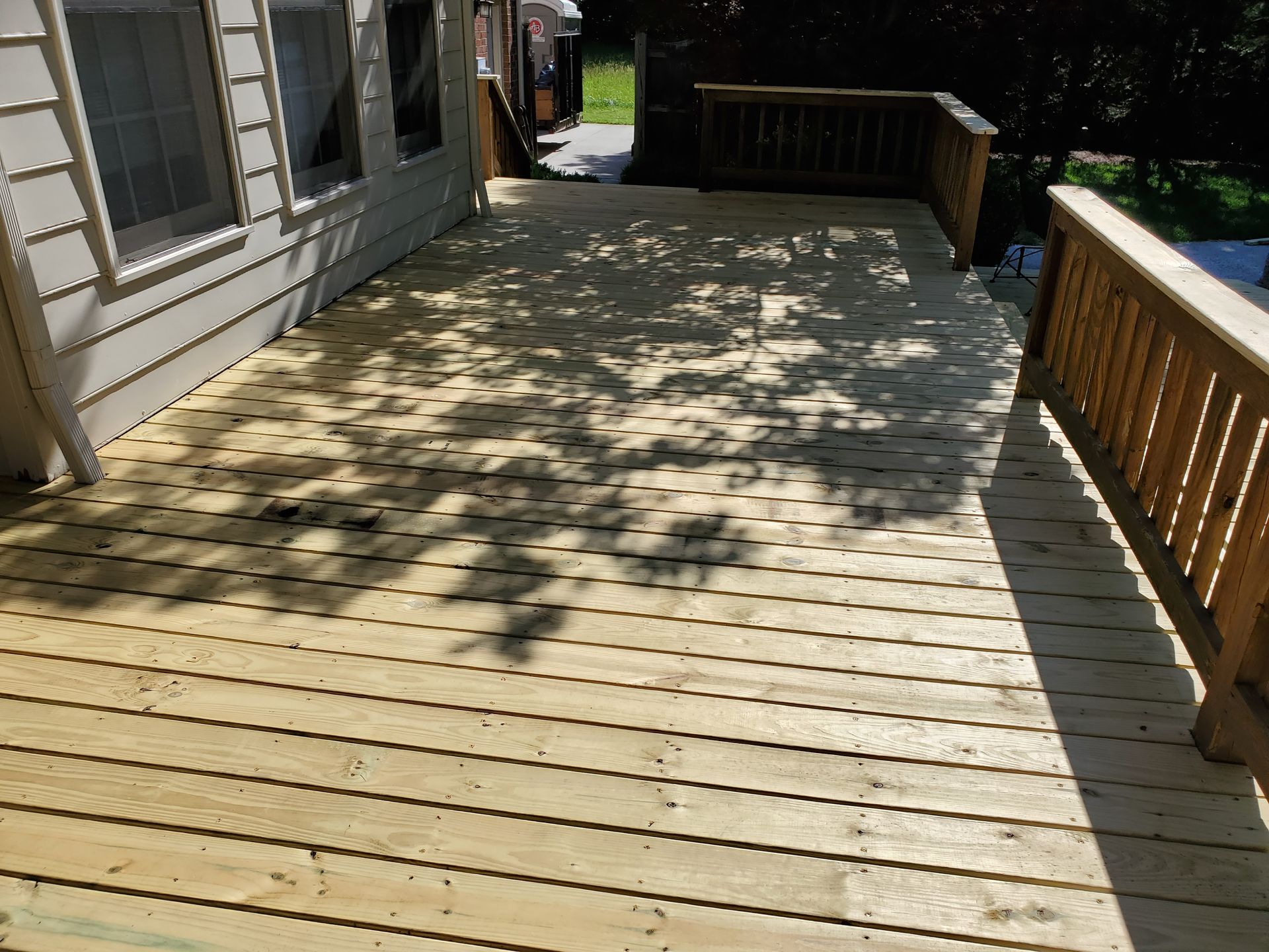 Wooden deck with tree shadows on a sunny day. Railing on the right, siding on the left.
