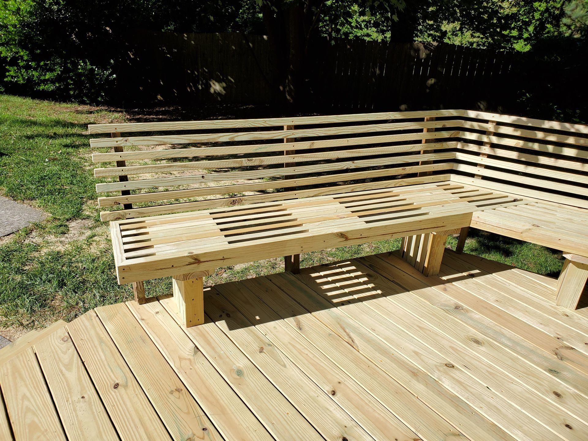 Wooden deck with built-in bench, backrests, and slatted seat. Sunny outdoor setting.
