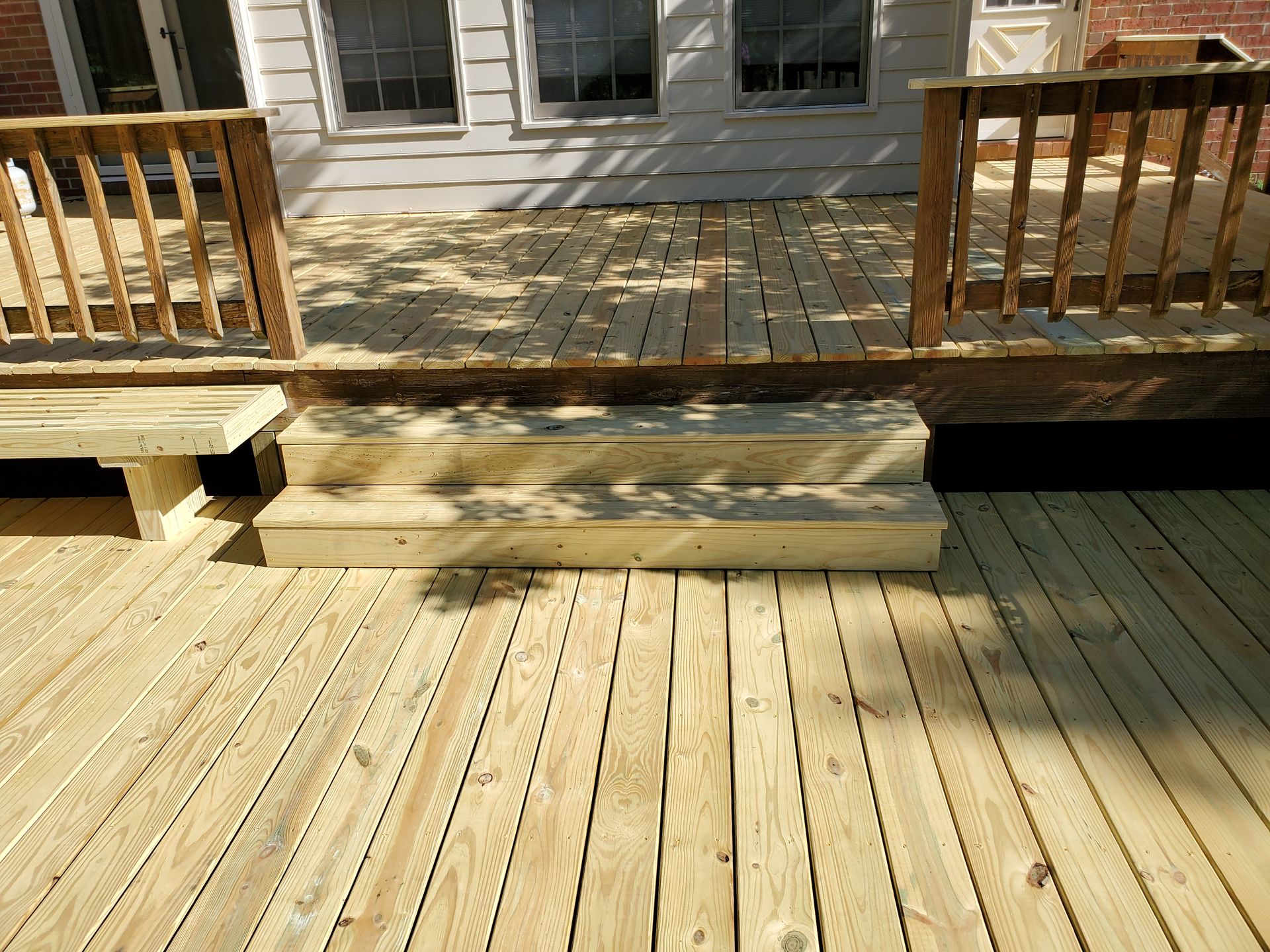 Wooden deck with steps, handrails, and a bench, leading to a house.