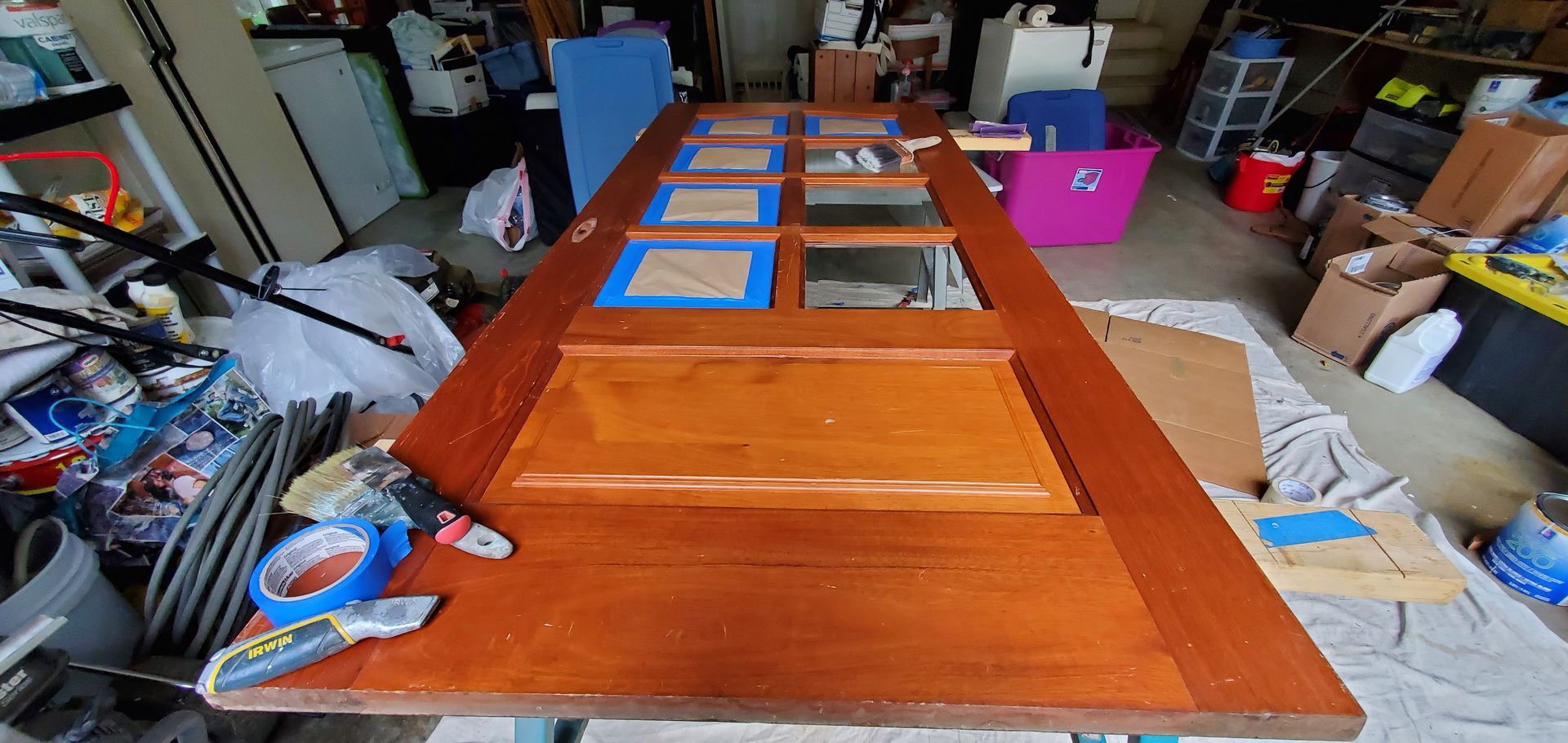 Wooden door being prepped for painting, taped around the glass panels. Garage setting.