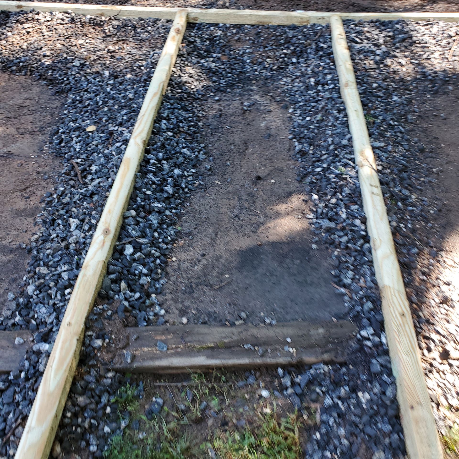 Wooden frame construction on gravel path. Two long beams with connecting crossbeams.